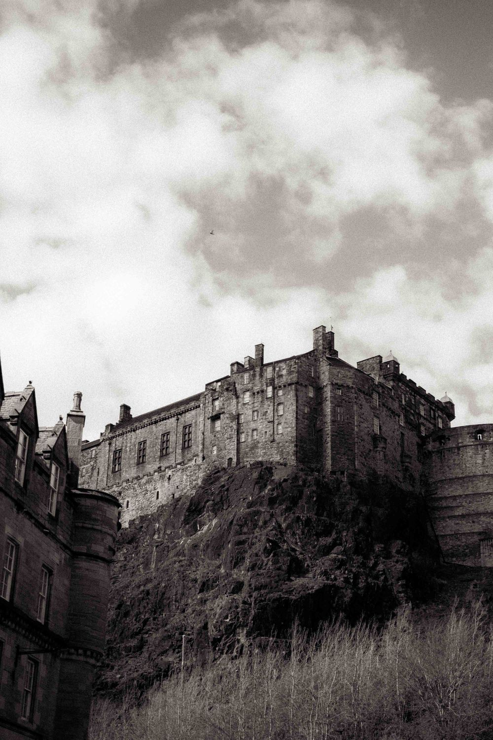 Dramatic black and white view of Edinburgh Castle perched on volcanic rock under cloudy skies.