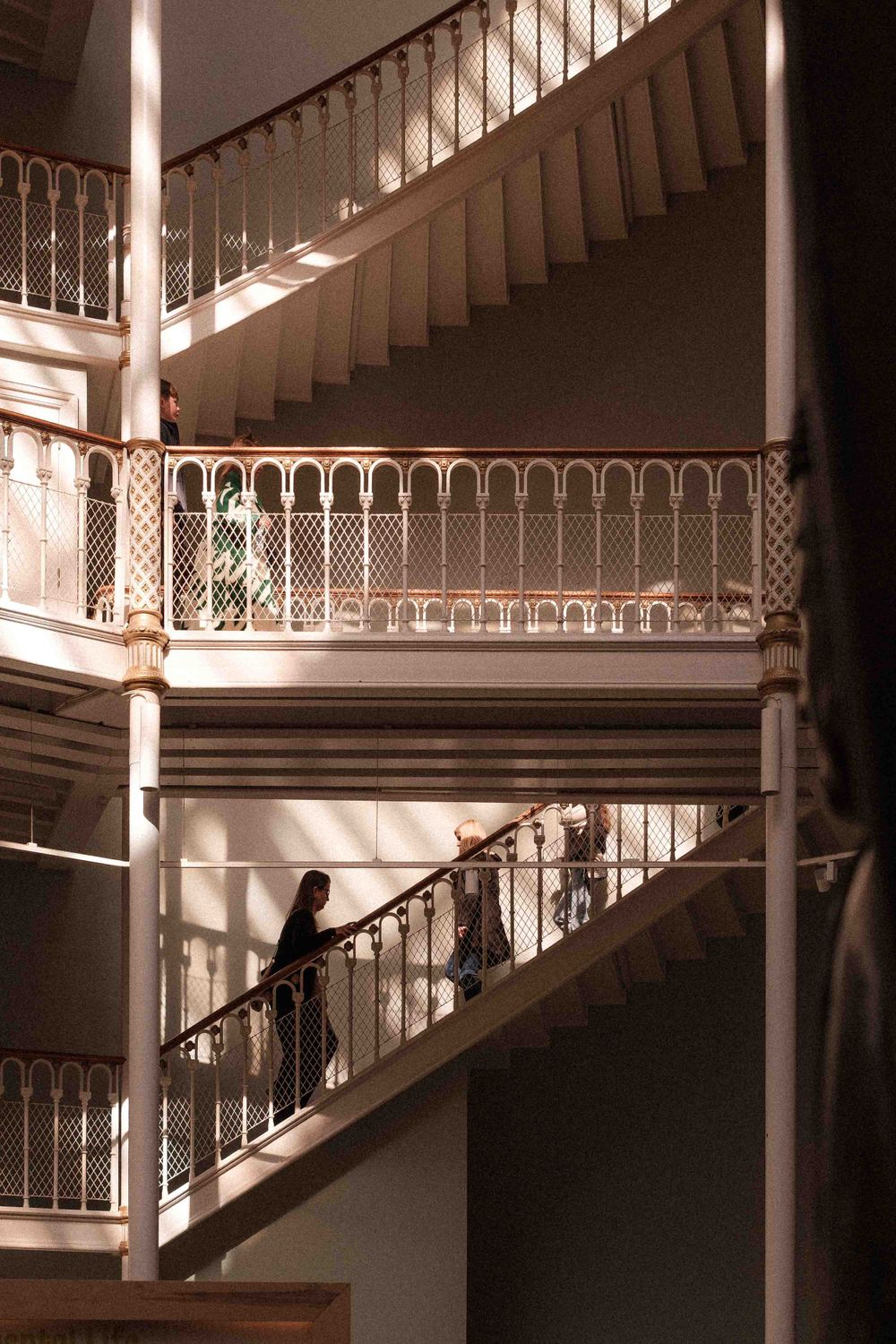 Sunlight streams through ornate iron railings on a grand white staircase in a historic building.