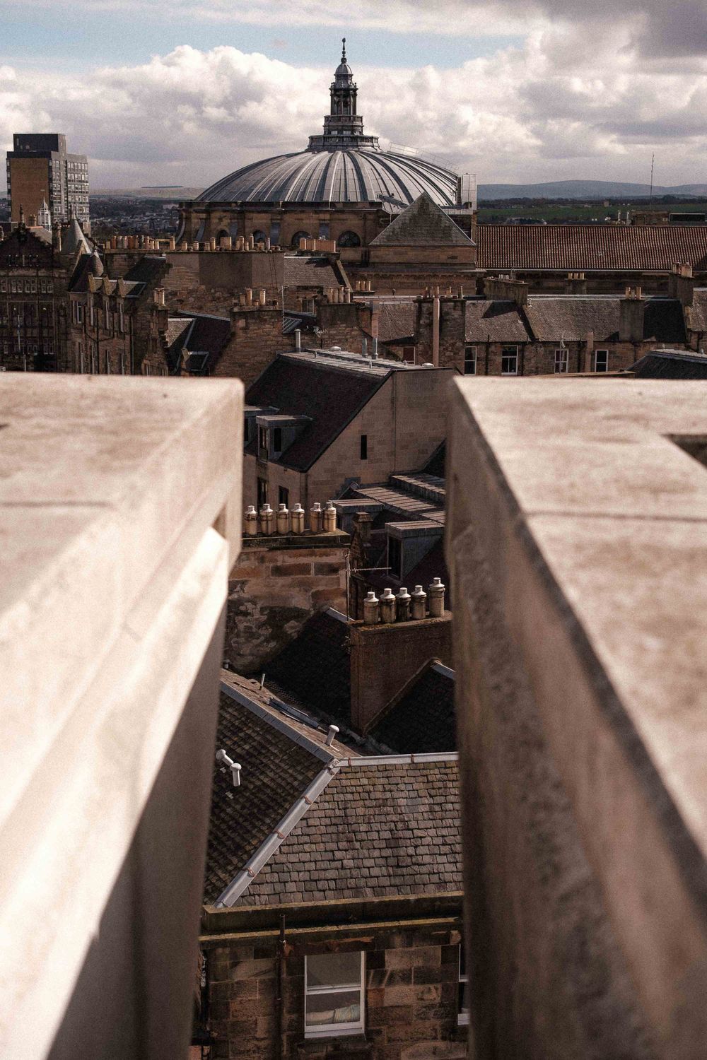 A domed building rises above Edinburgh's historic skyline with dramatic cloudy skies overhead.