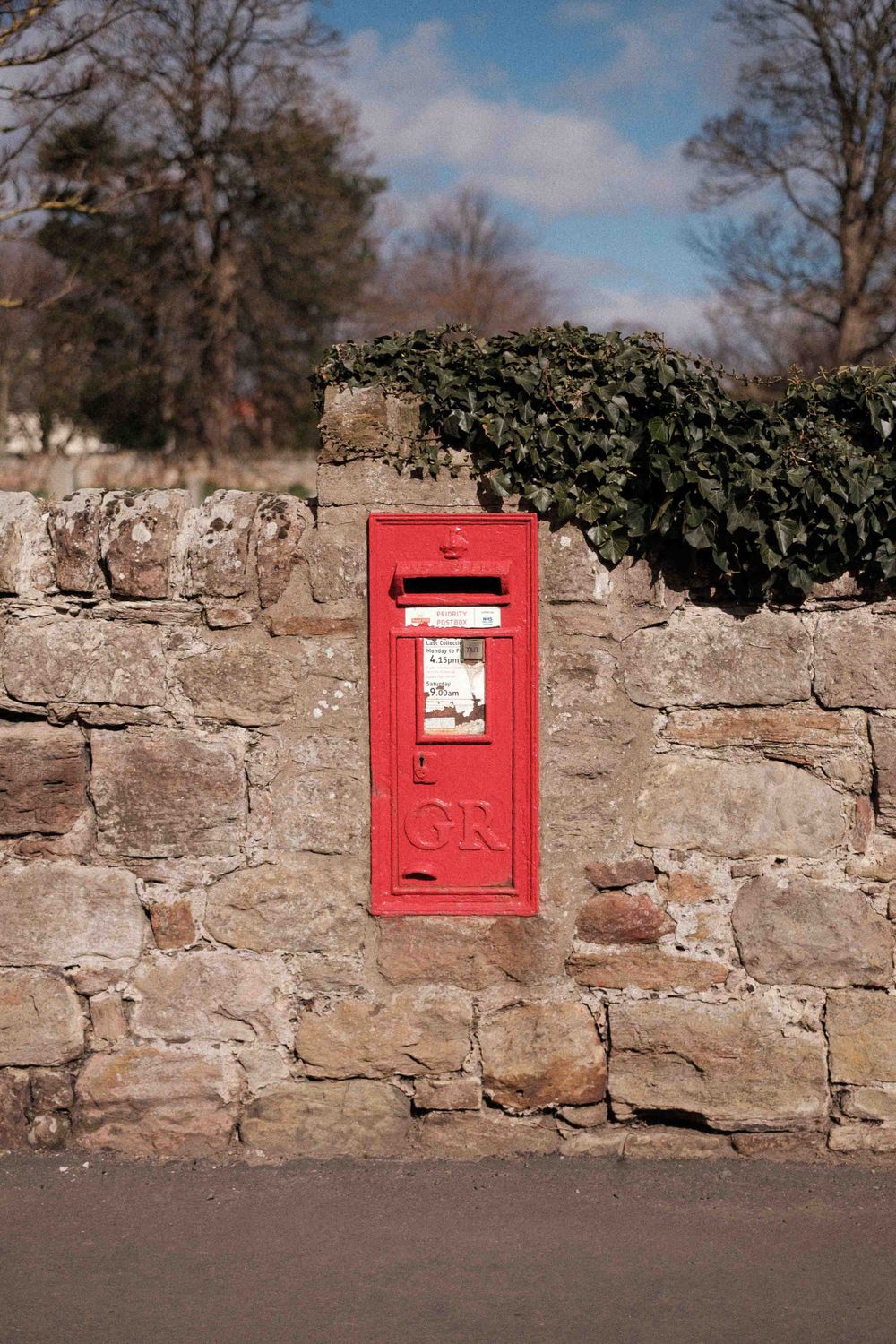 Traditional red British Royal Mail postbox embedded in an old stone wall.