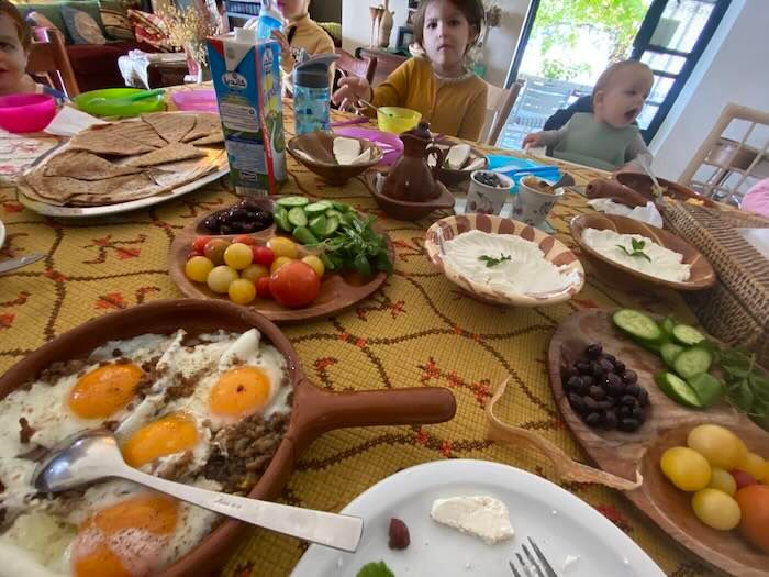 A colorful Mediterranean style brunch spread on a patterned tablecloth with eggs, vegetables, dips, and breads.