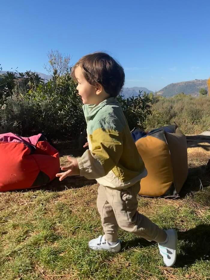 Small child plays outdoors against a scenic mountain backdrop wearing a two-toned shirt and light pants on a sunny day.