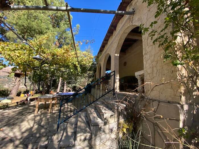 Mediterranean stone villa with arched entrance and climbing vines seen from a sunlit garden path.