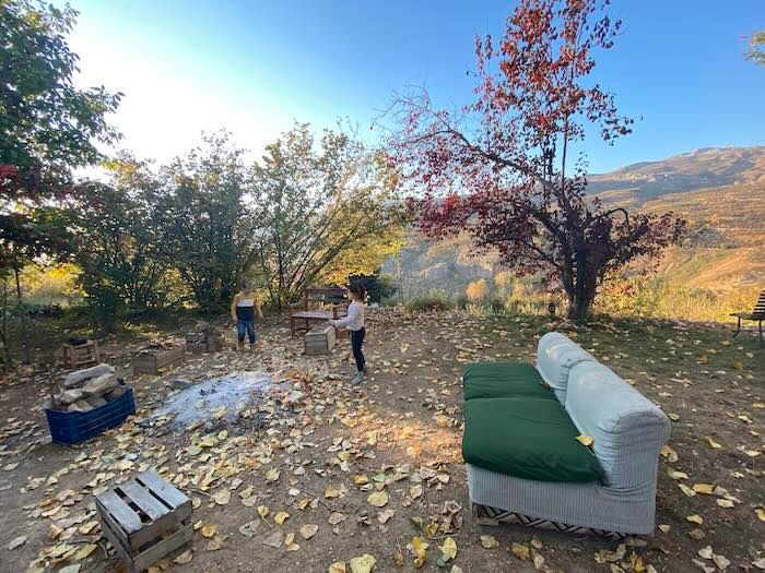 An outdoor seating area with a green couch surrounded by fall foliage and mountain views in the background.