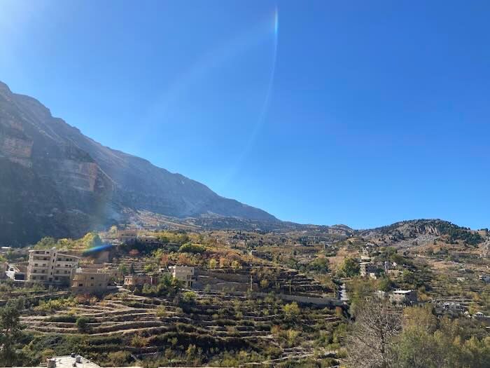 Terraced mountain landscape under bright blue skies with scattered buildings dotting the steep hillside.