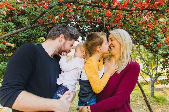 A loving family shares joyful moments together outdoors under vibrant red blossoming trees during autumn.