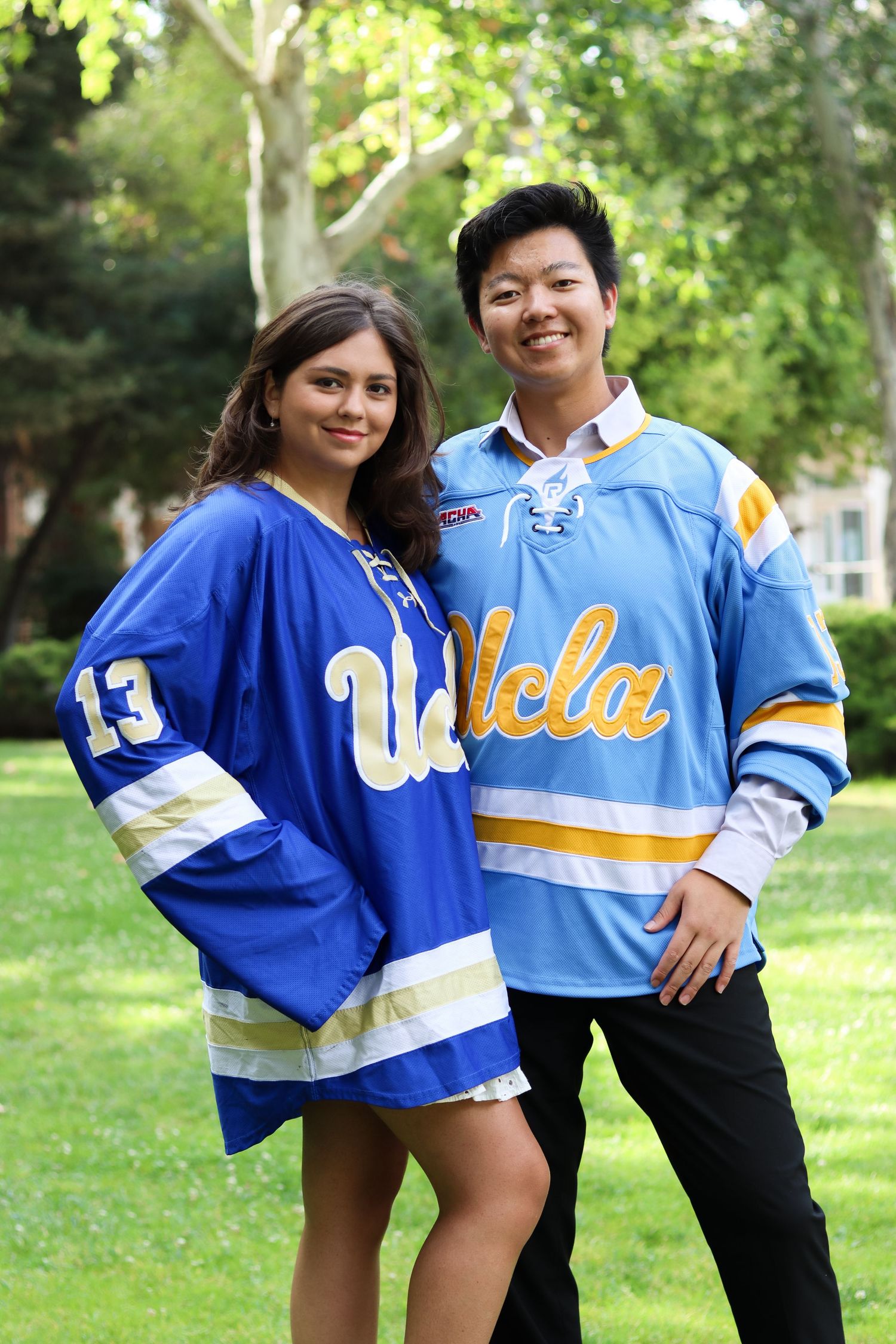 Group wearing UCLA sports jerseys pose together on grass field.