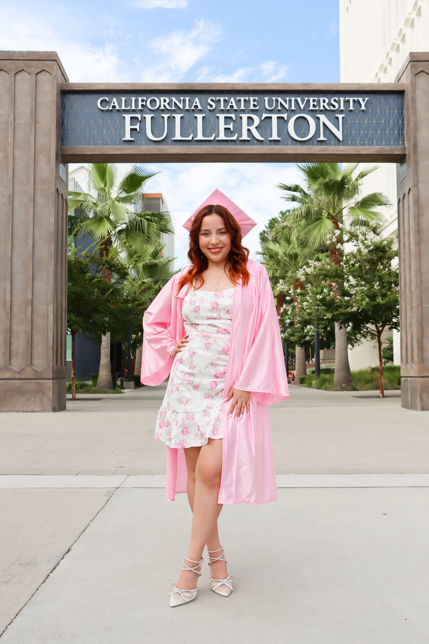 Graduate in pink robe poses in front of California State University Fullerton entrance sign.