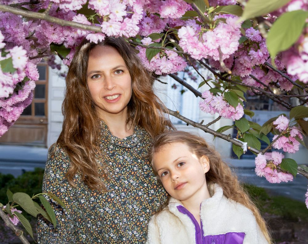 Two people pose together under beautiful blooming pink cherry blossoms on a spring day.