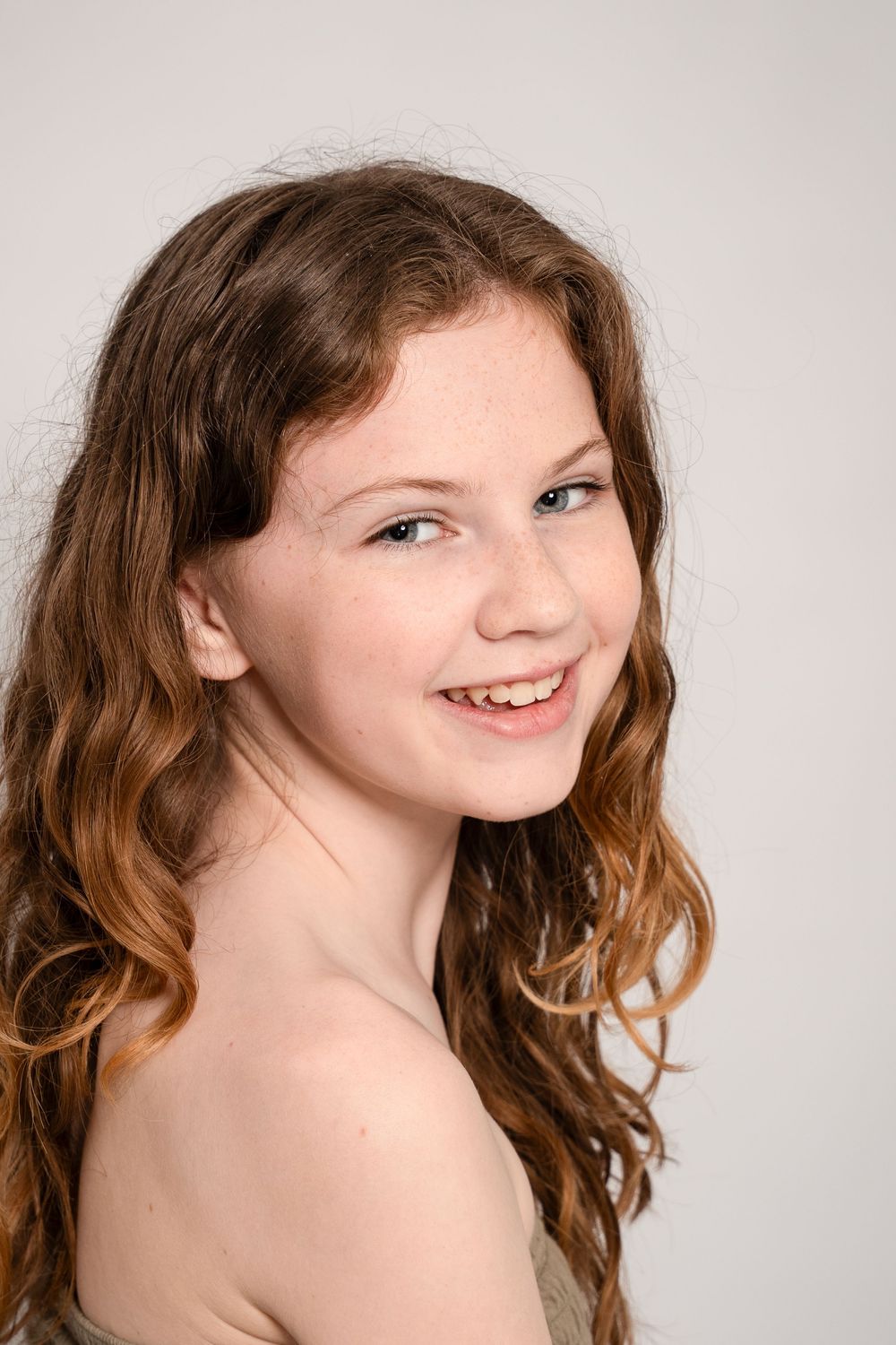 Portrait of someone with long wavy brown hair and a bright smile against a light gray background.