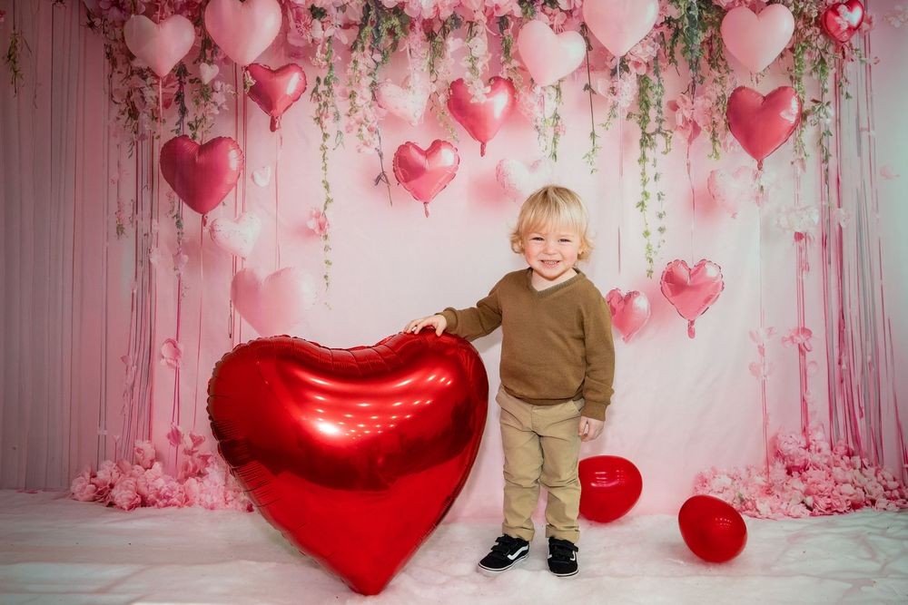 Valentine's day photo setup with pink and red heart balloons, floral decorations and a large metallic red heart balloon.