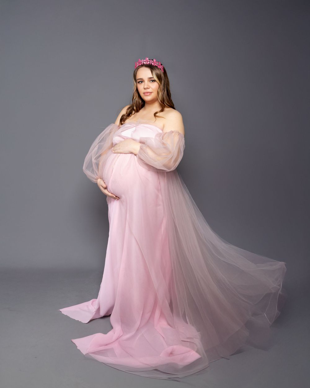 A dreamy maternity portrait in Aberdare studio in a soft pink tulle gown with floral headpiece against gray background.