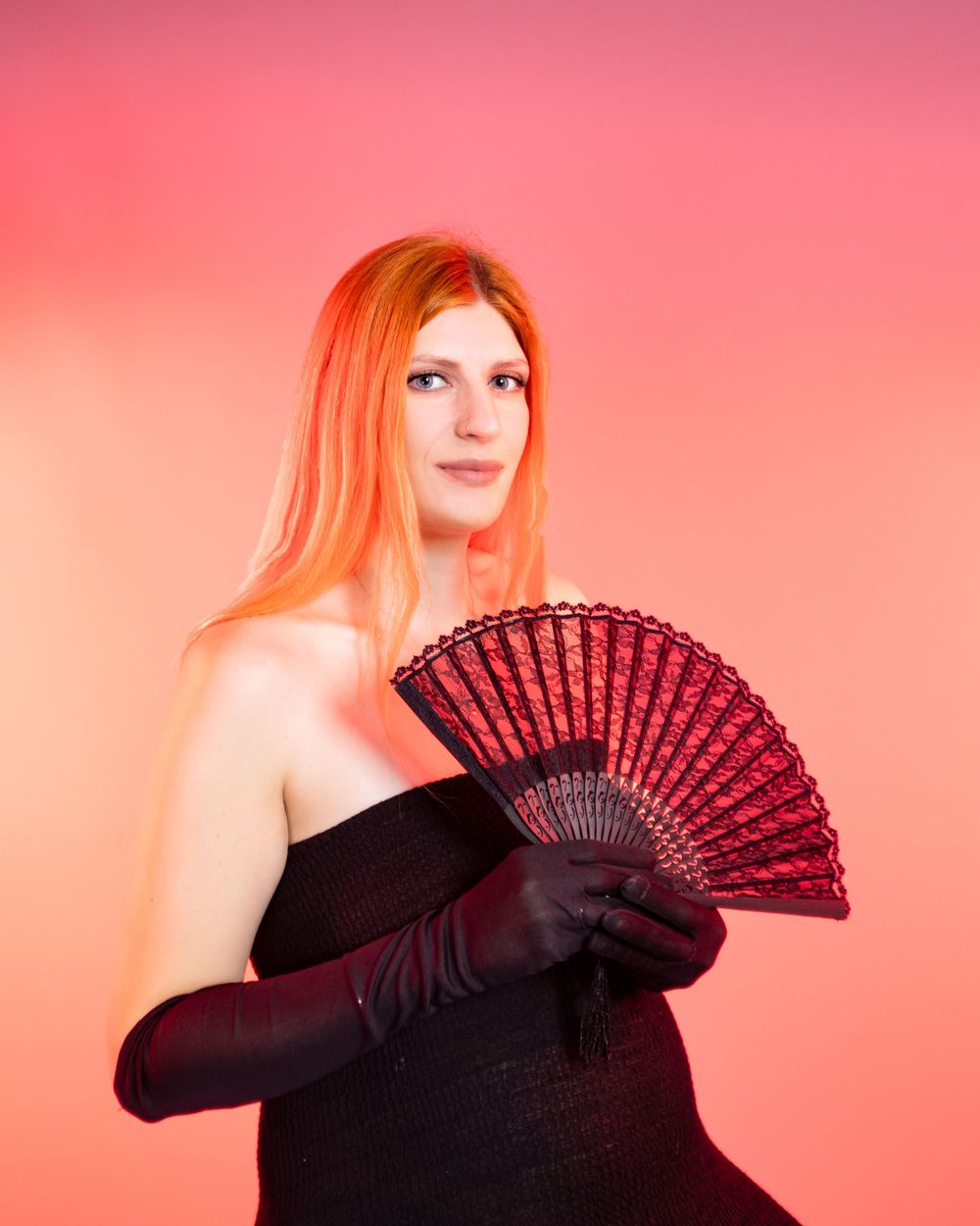 Dramatic portrait with black dress and burgundy fan against coral pink backdrop.