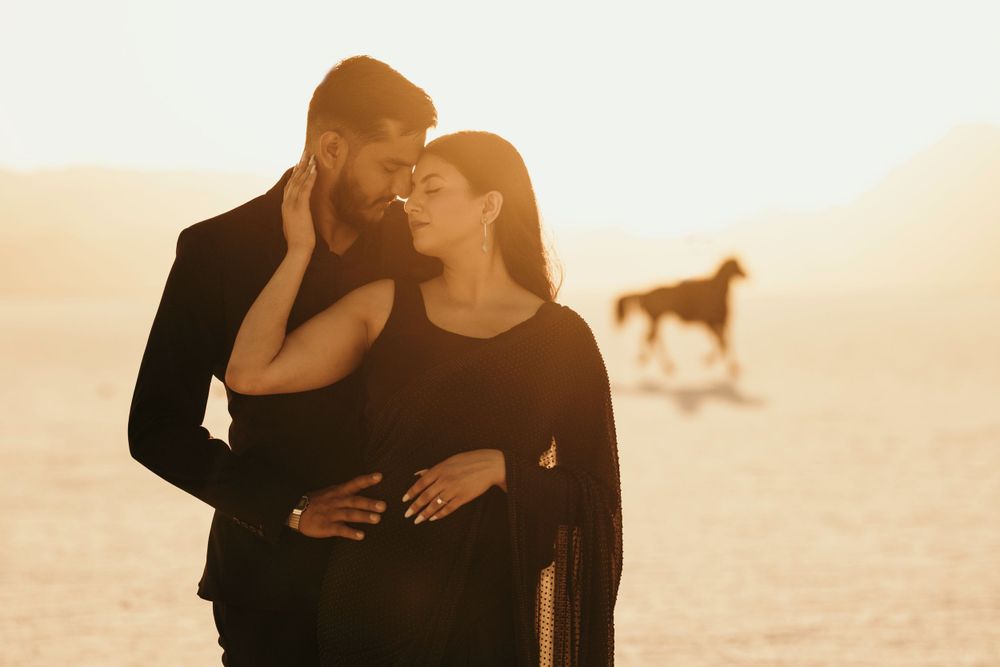 Romantic couple share an intimate moment in desert scenery with horse silhouette in background at golden hour.