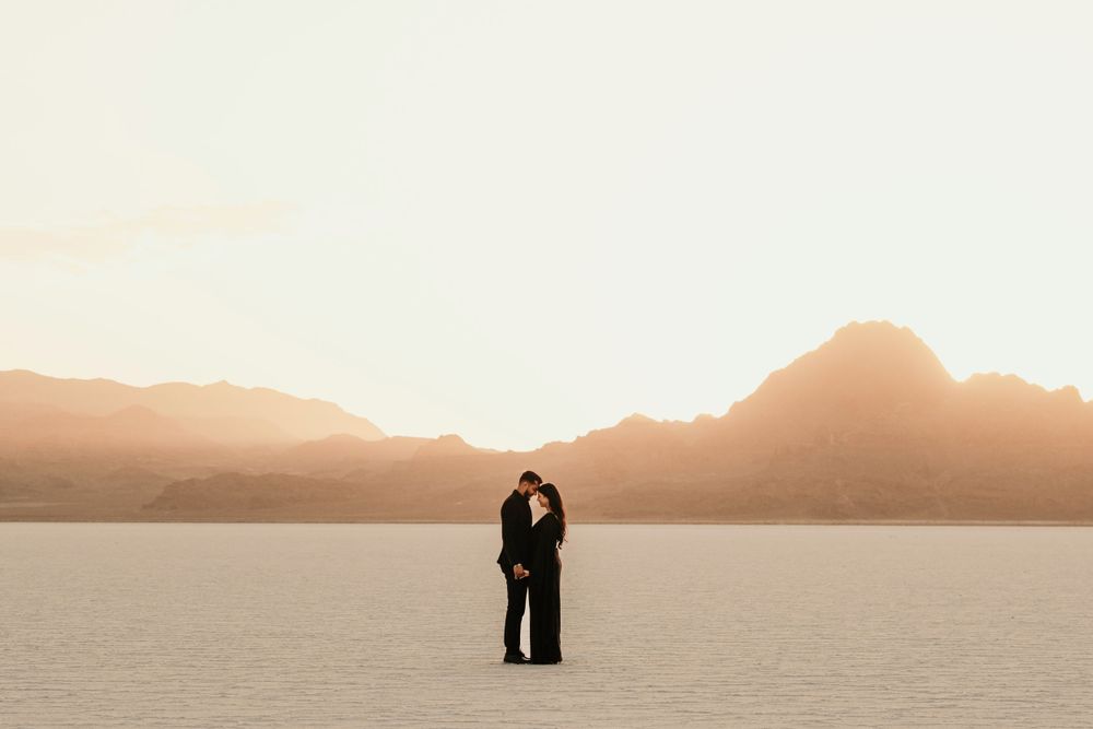 A silhouetted couple embracing on a salt flat at sunset with mountains in the background.