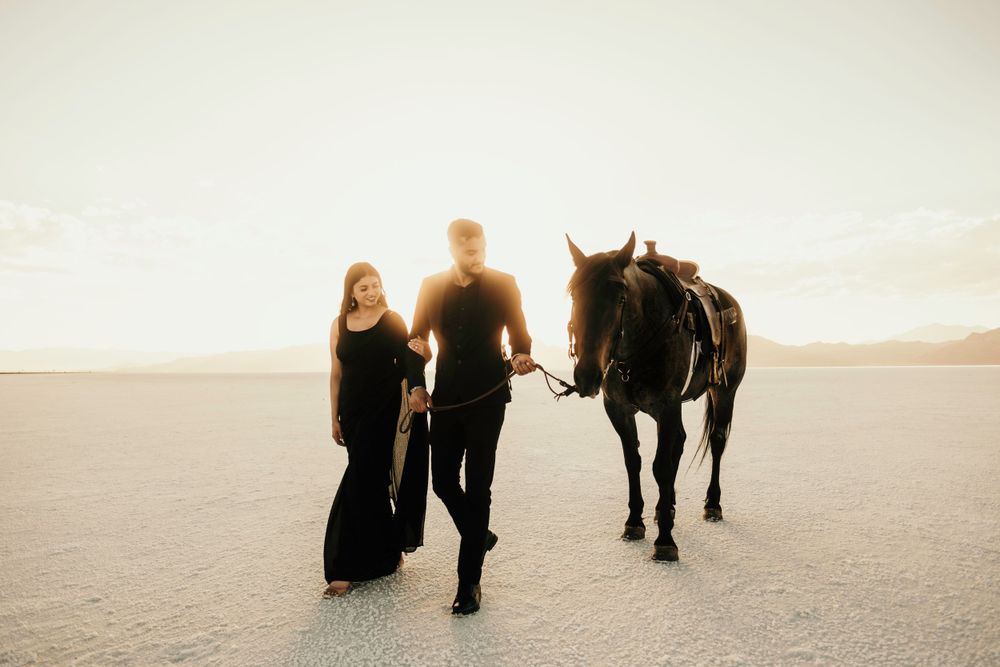 A romantic couple in black attire walking with their horse on a desert plain during golden hour.