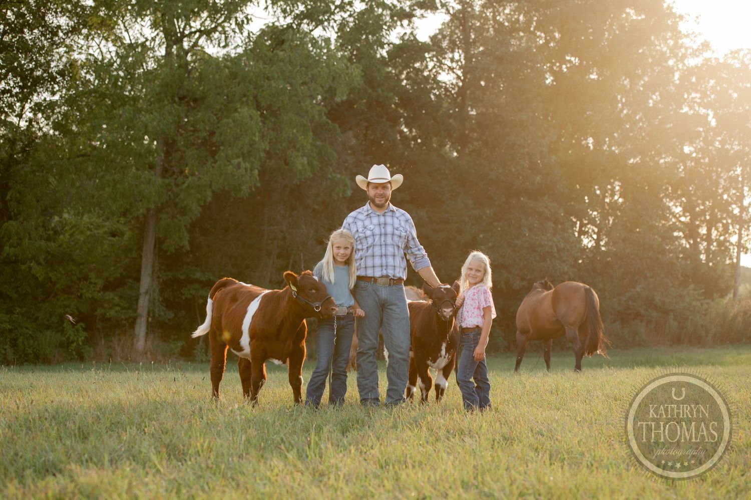 People and horses gather in a pastoral field during golden hour.