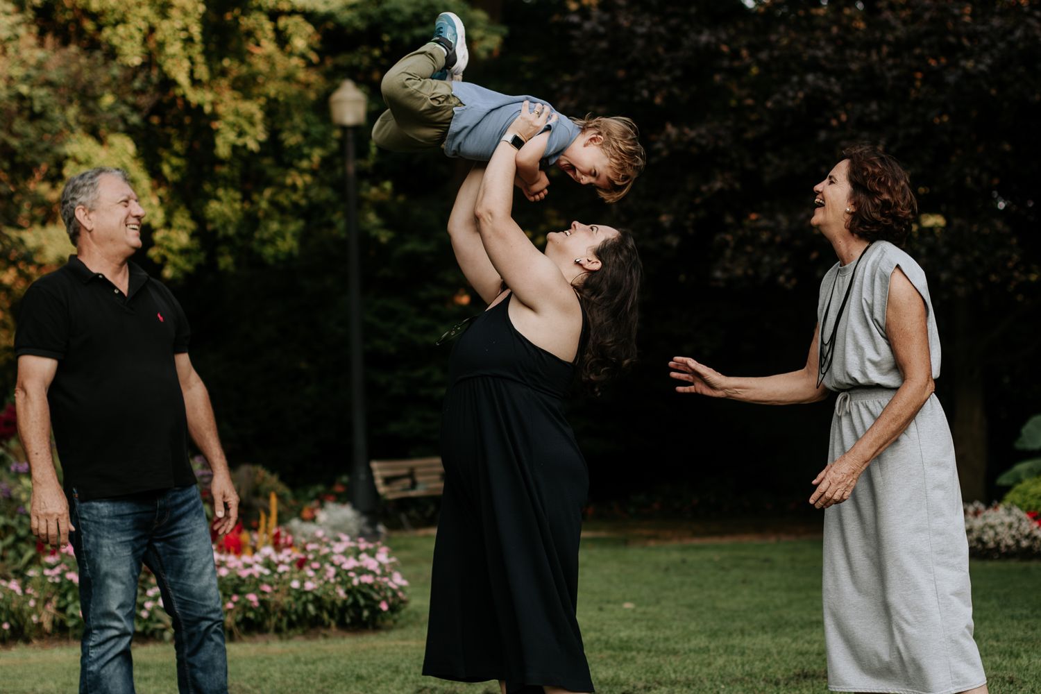 grandparent looking at their daughter lifting up her son at the park, in Toronto