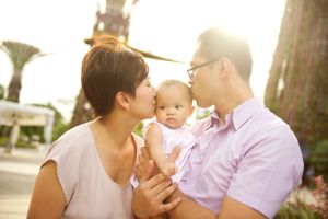 Mom kissing her baby while dad smiles photographed outdoors by Phoebe Lee Photo in Toronto