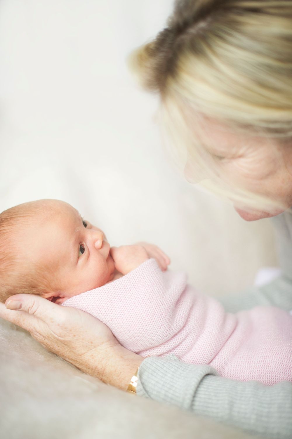 Blonde mother gazing down at her pink-swaddled newborn, taken by Phoebe Lee Photo in a natural light session in Toronto