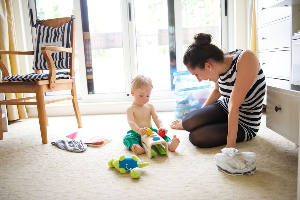 Toddler sitting on the floor with toys while mom watches, captured by Phoebe Lee Photo in a bright Toronto home