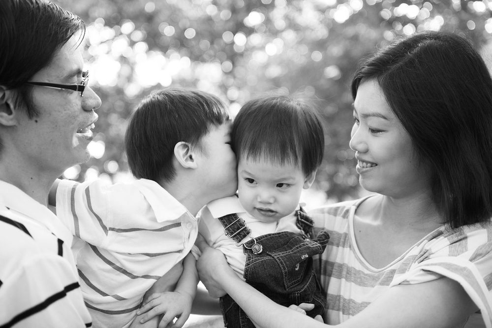 Parents holding their toddler in a Toronto park, smiling in a black-and-white family portrait by Phoebe Lee Photo