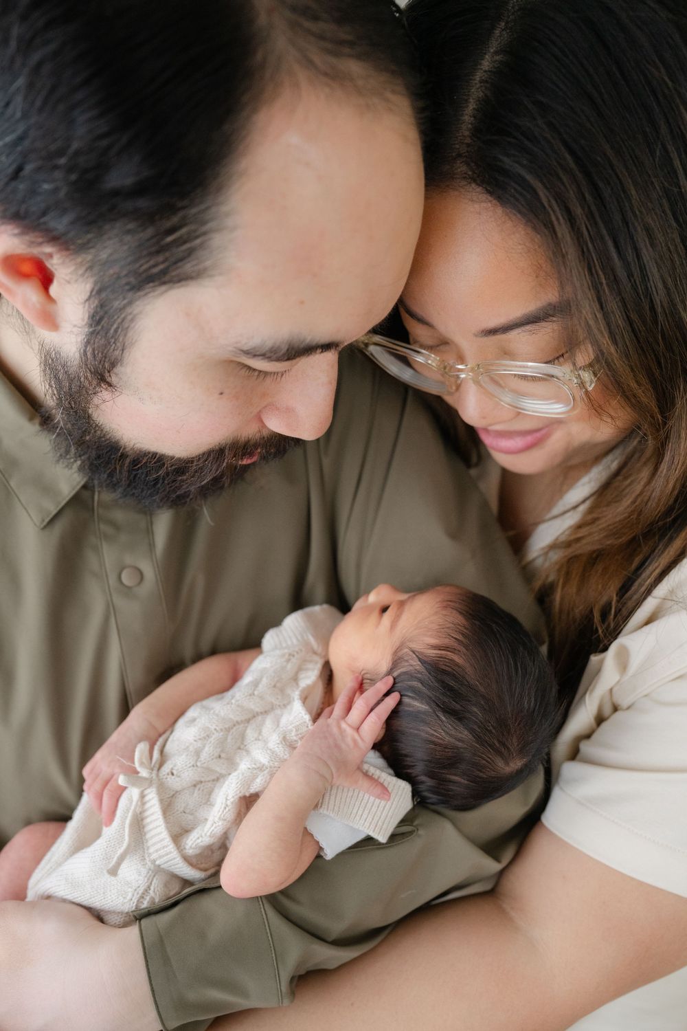 Mom and Dad gazing lovingly at newborn baby looking cozy. Photographed by GTA family newborn photographer Phoebe Lee Photo. Toronto baby.