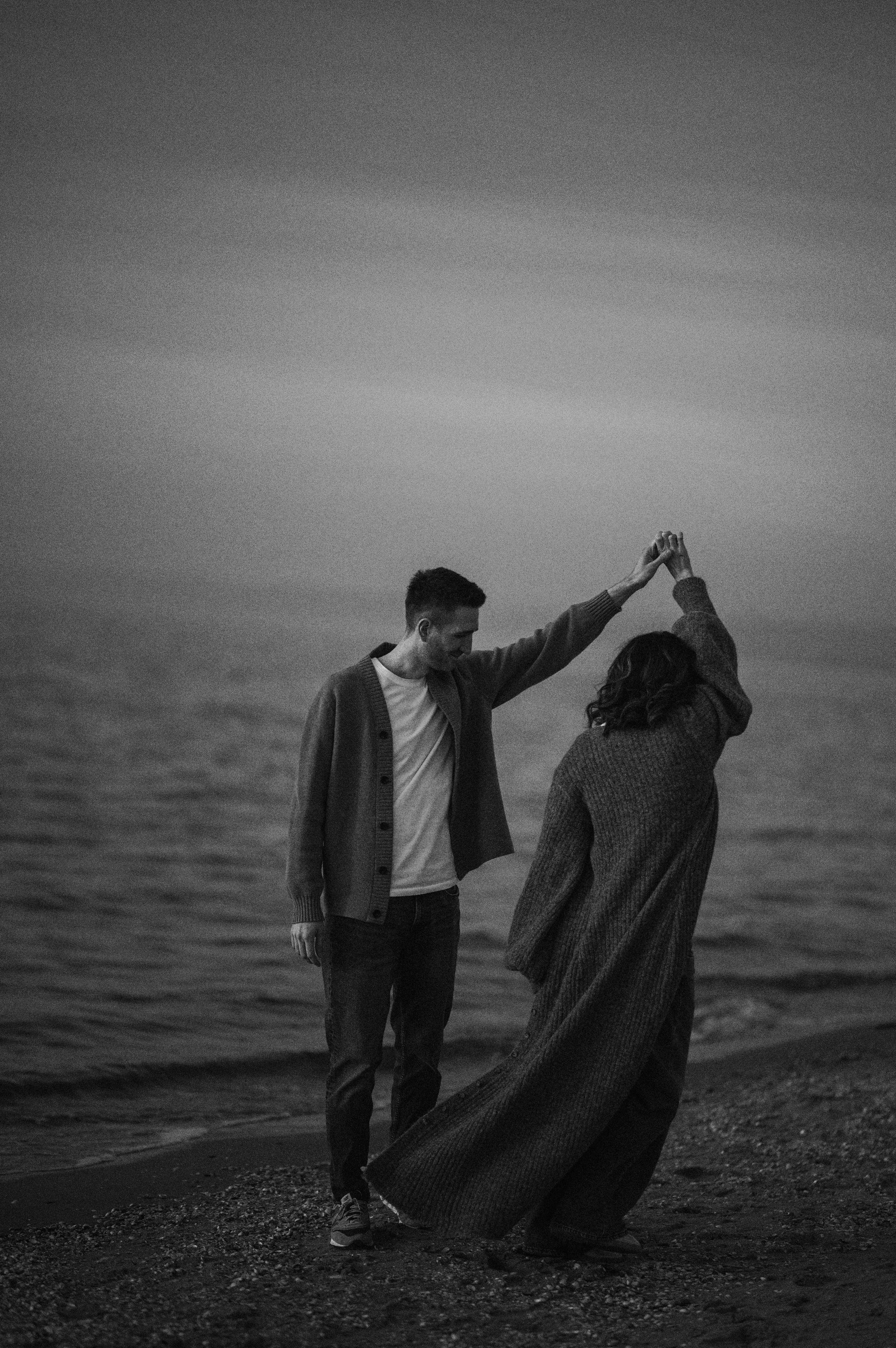 A couple dances together on a beach at sunset in black and white photography.