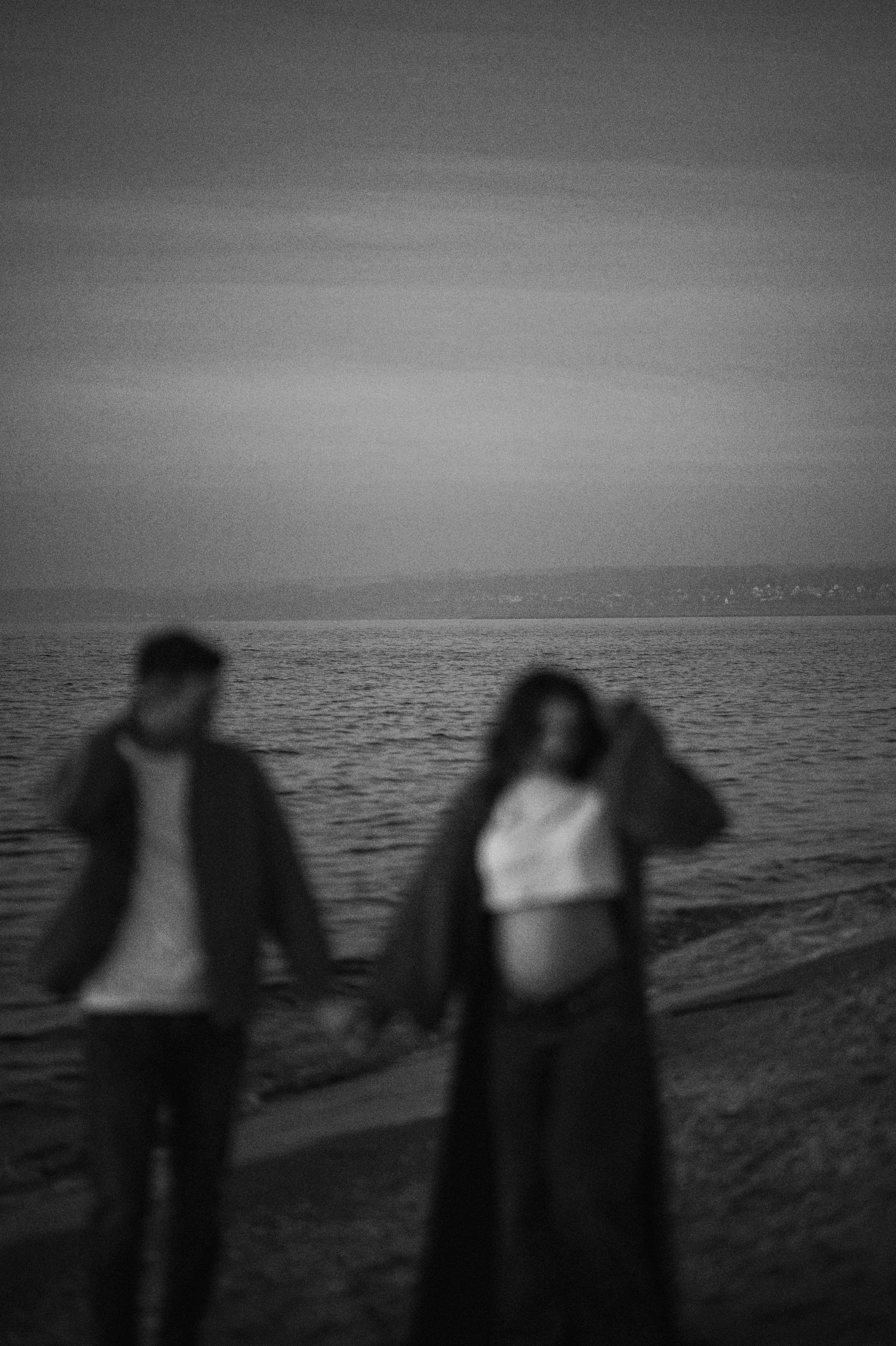 Silhouetted figures stand on a beach against a hazy ocean backdrop.
