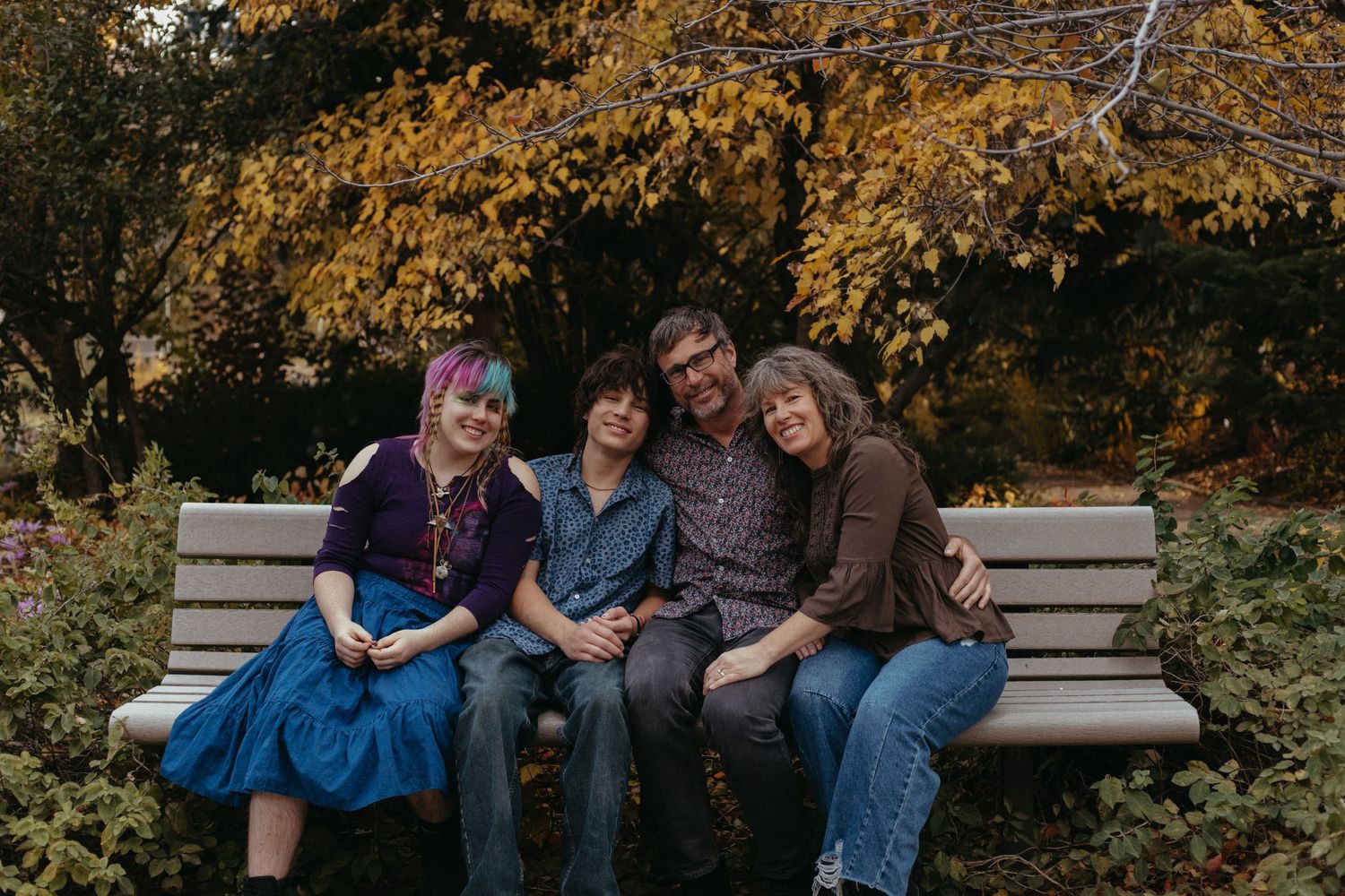 A family sitting together on a wooden bench during an autumn photo session.
