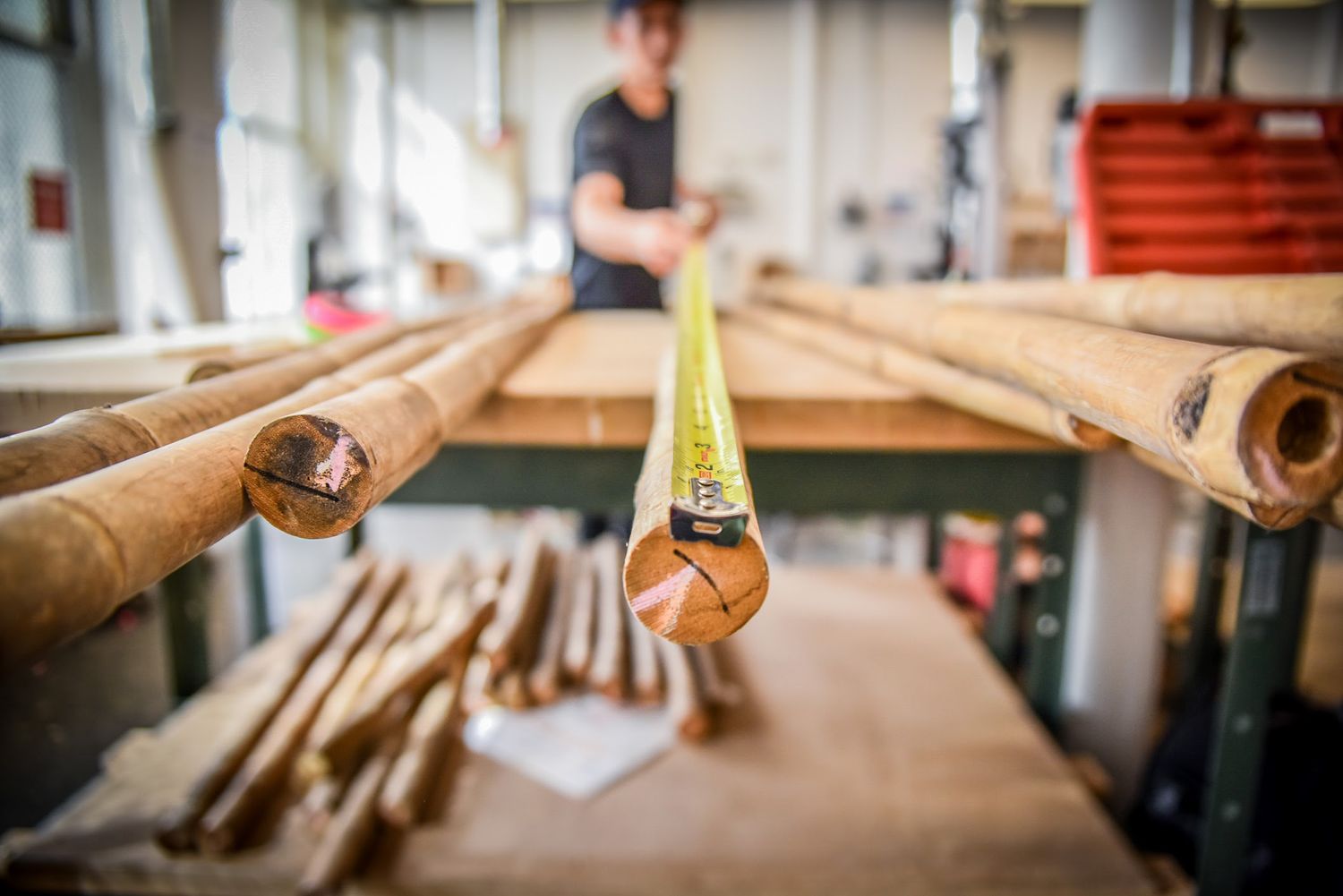 Measuring tape rests on wooden bamboo poles in a carpentry workshop with tools and equipment in the background.