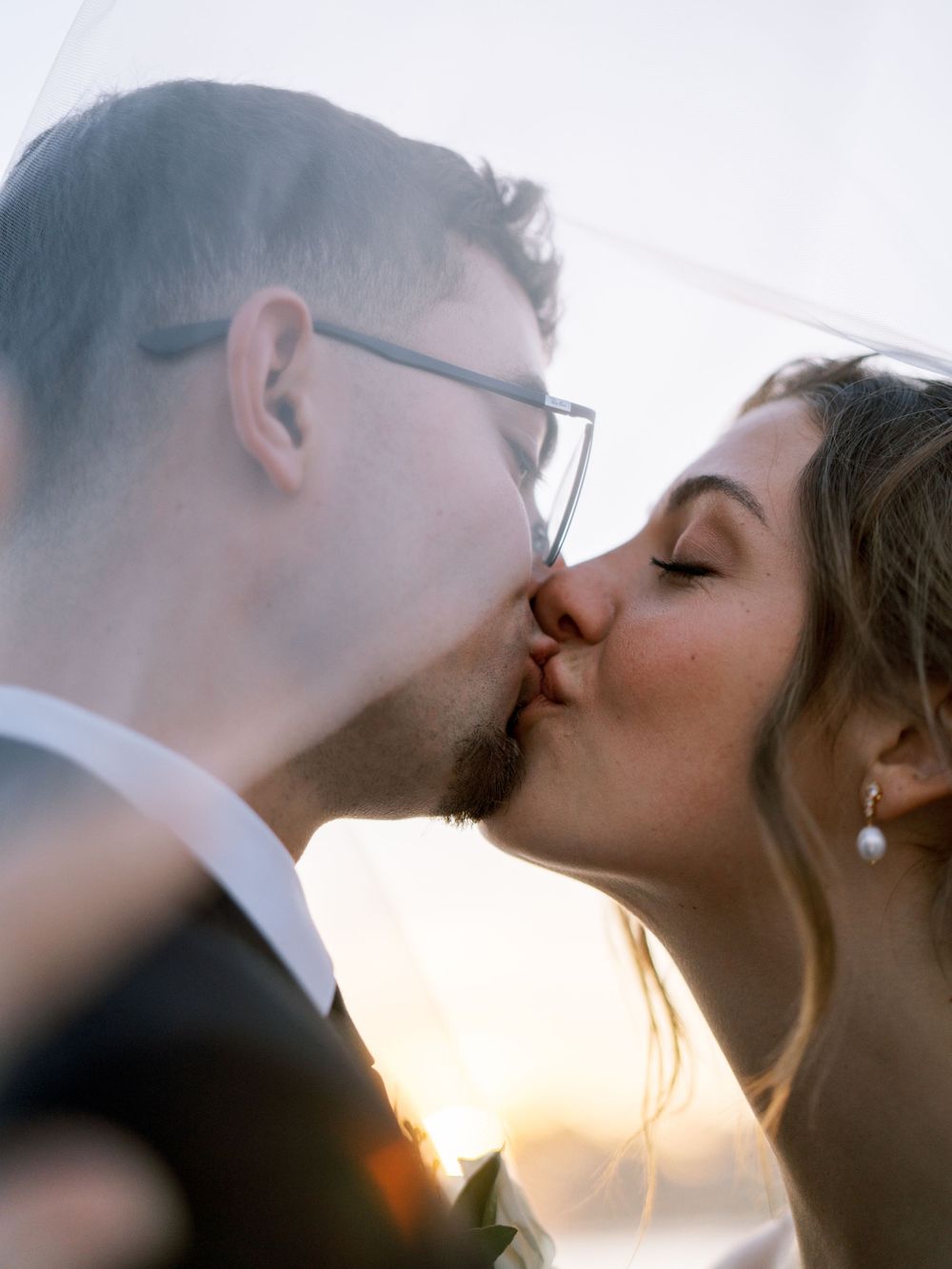 An intimate wedding kiss captured during golden hour with soft sunlight creating a romantic glow.