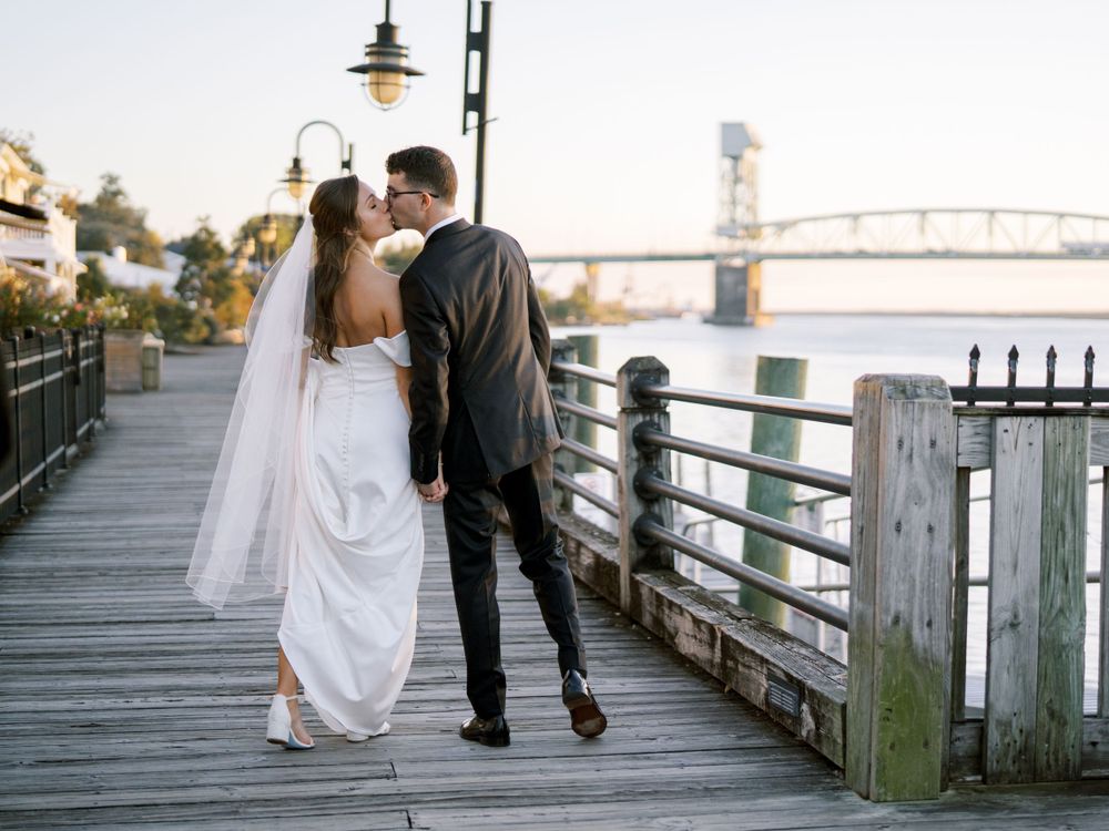 Newlyweds sharing an intimate moment on a wooden boardwalk with a bridge visible in the background.