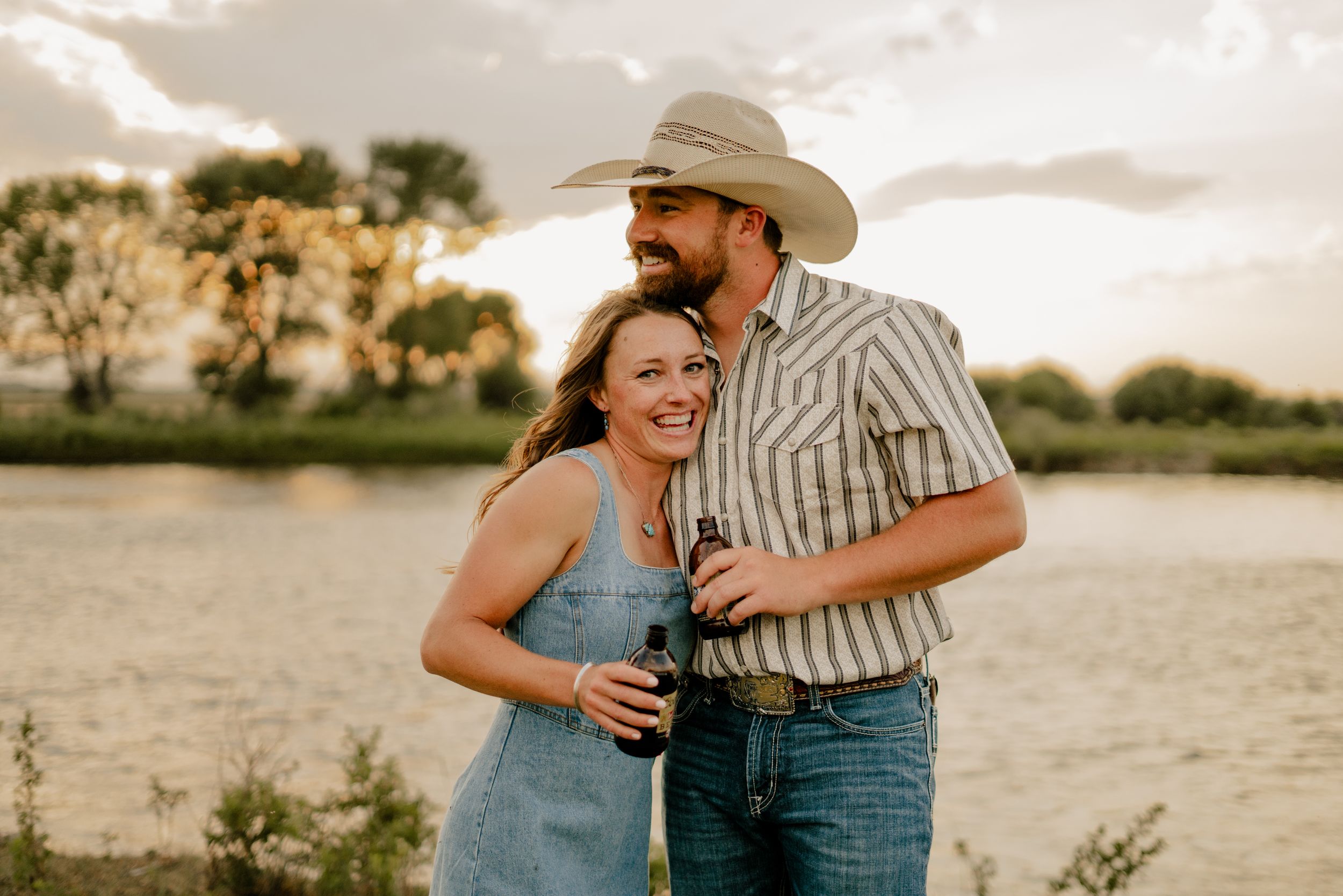 A young couple laughing and holding each other in a tender embrace with the sunset and river behind them