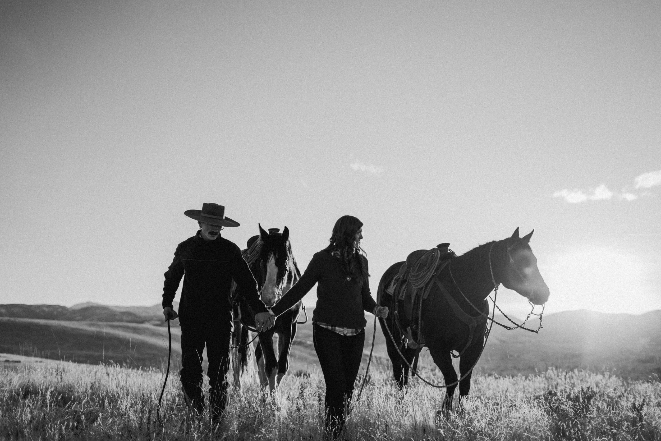 A black and white image of a couple leading two horses