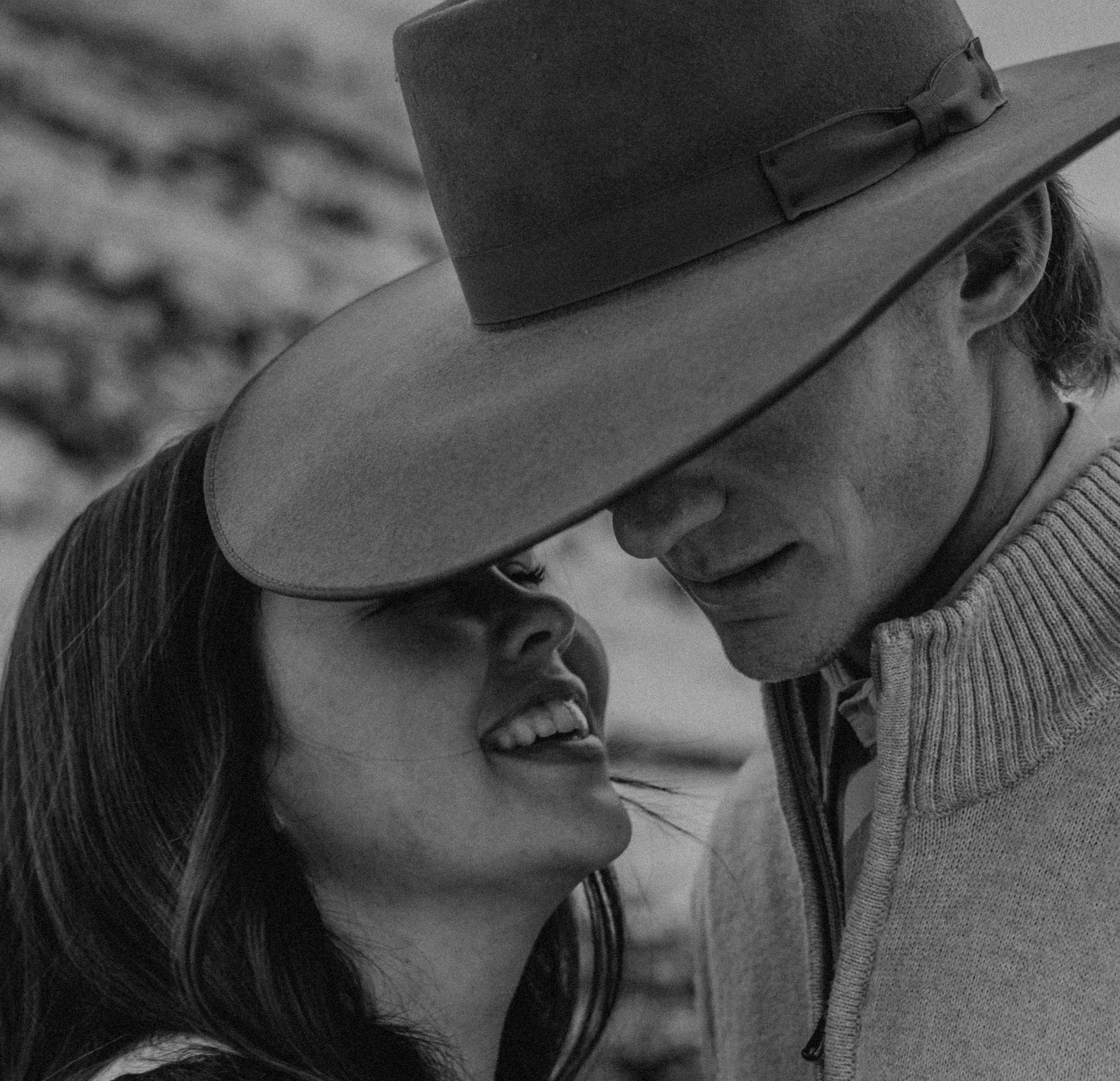 A black and white image of a couple with the man wearing a cowboy hat and the woman smiling adoringly at the man