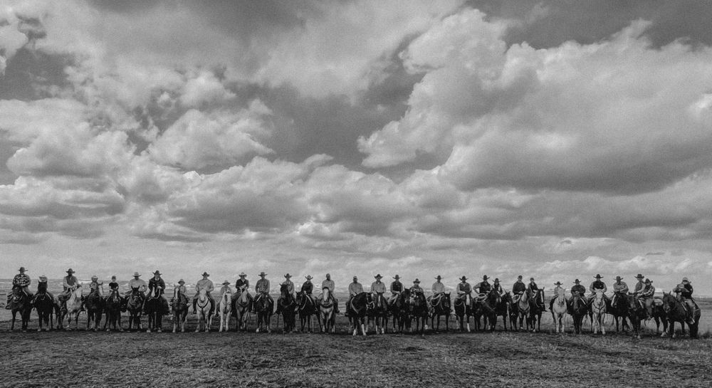 Over 30 cowboys and cowgirls in a row with the mountains in the background