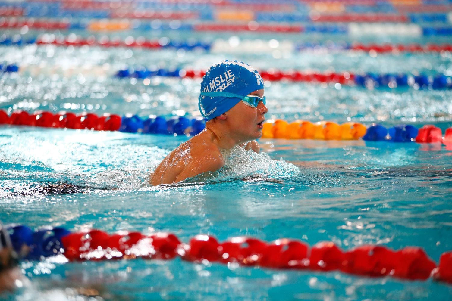 Swimmer performing breaststroke during competitive race in a pool with colored lane markers.