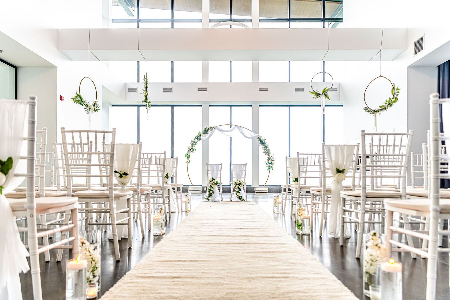 "Décoration élégante de cérémonie de mariage avec chaises blanches, bougies et arche florale, capturée par Payo Studio dans un cadre lumineu