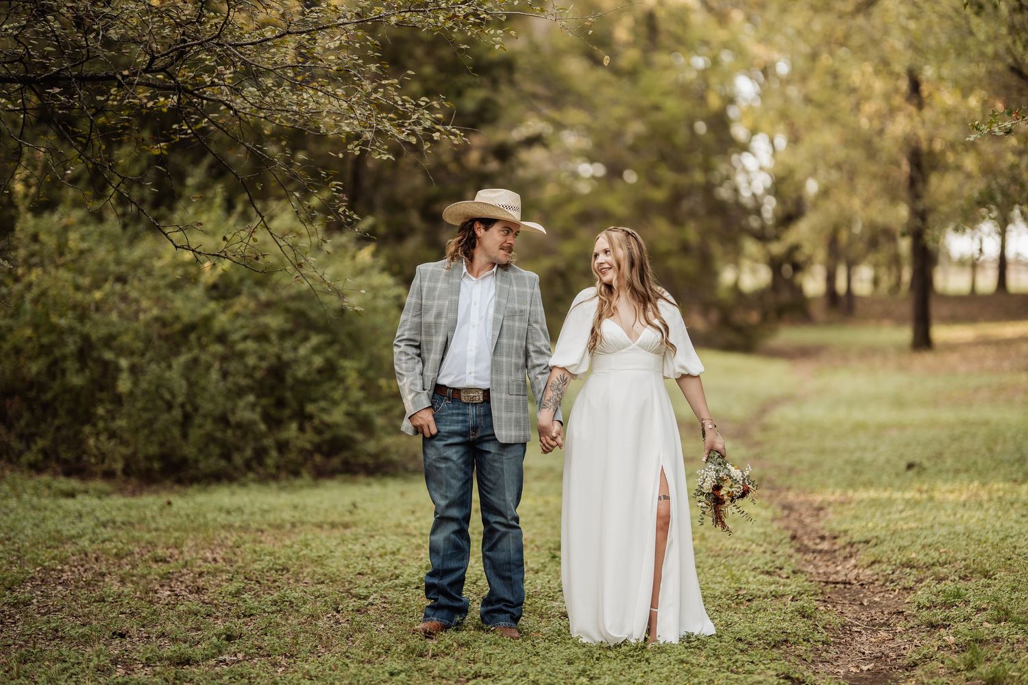 A romantic countryside wedding portrait of a couple walking together through a scenic field.