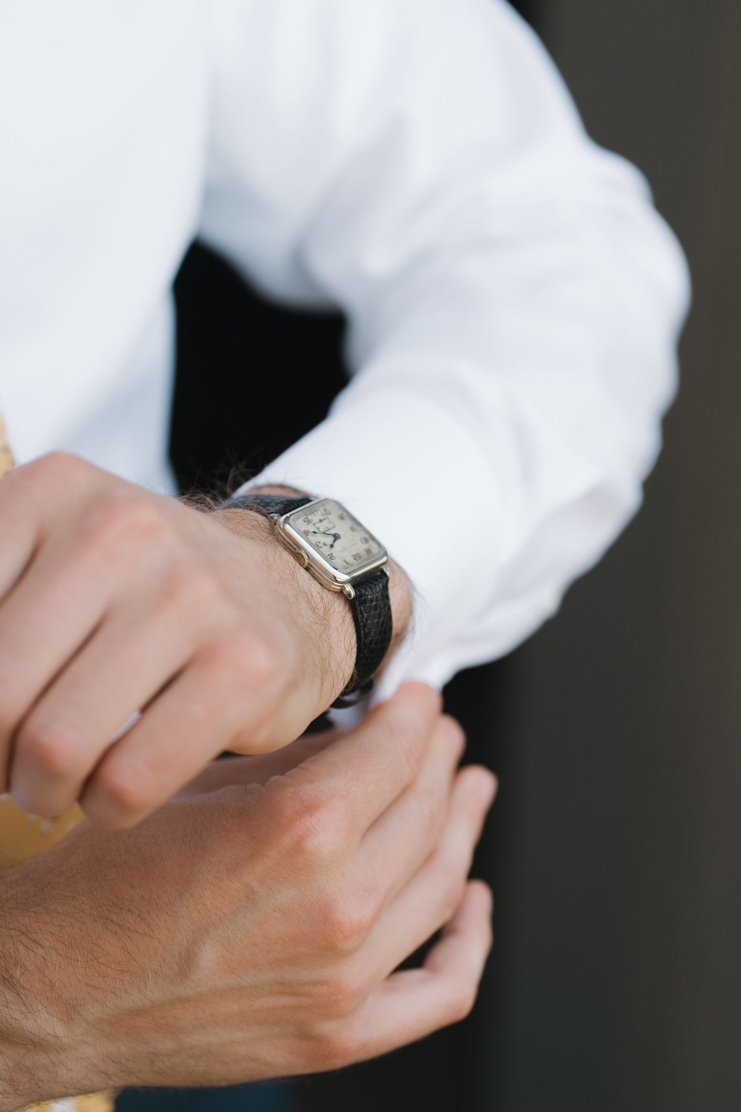 Close-up of hands adjusting a classic wristwatch with white shirt cuff.