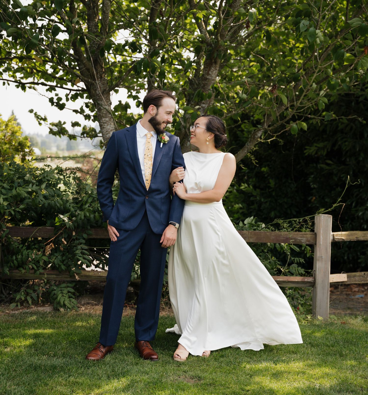 Wedding couple shares a joyful moment together outdoors by a wooden fence.