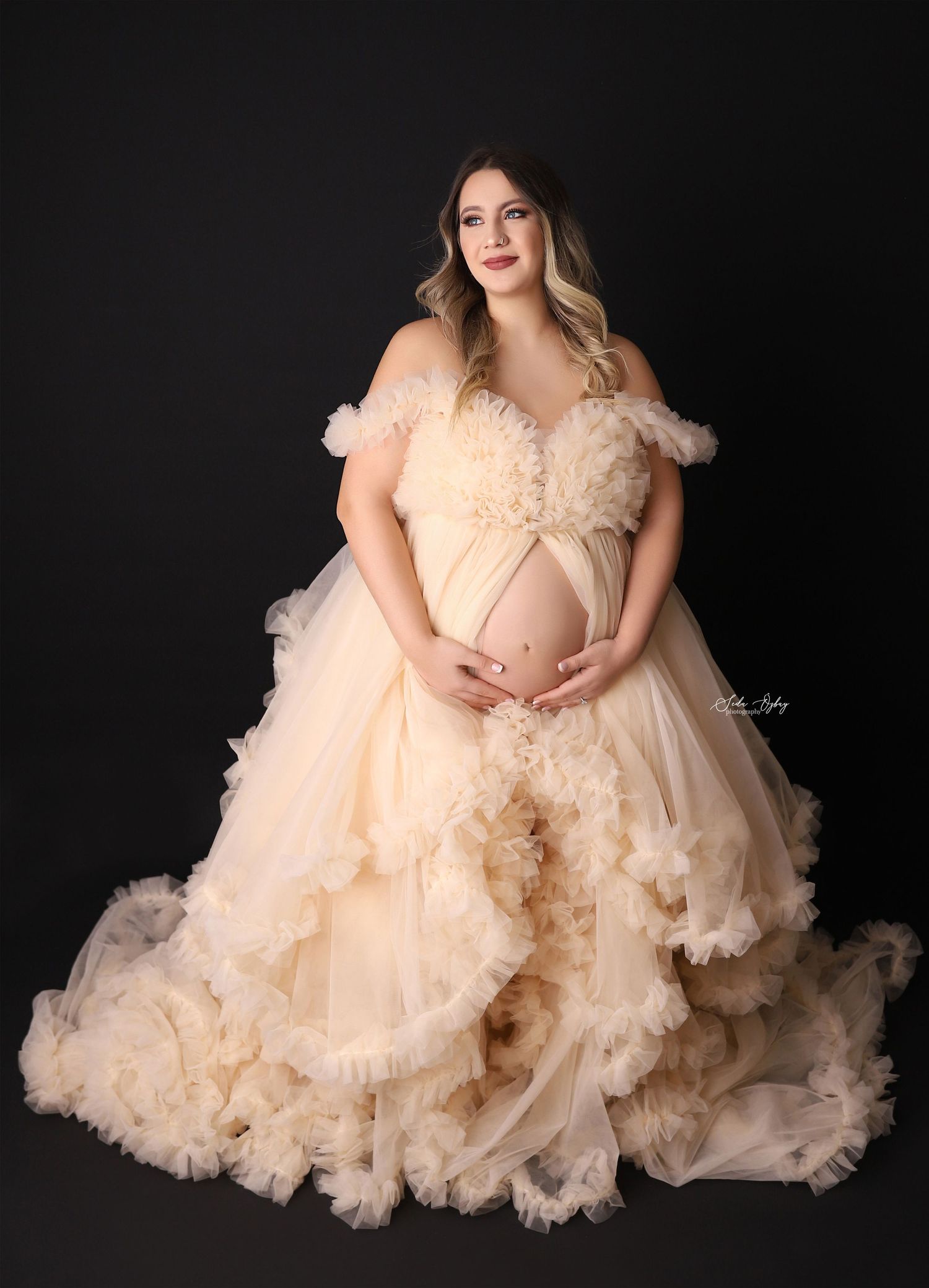 A luxurious champagne-colored maternity gown with ruffled details against a dark backdrop.