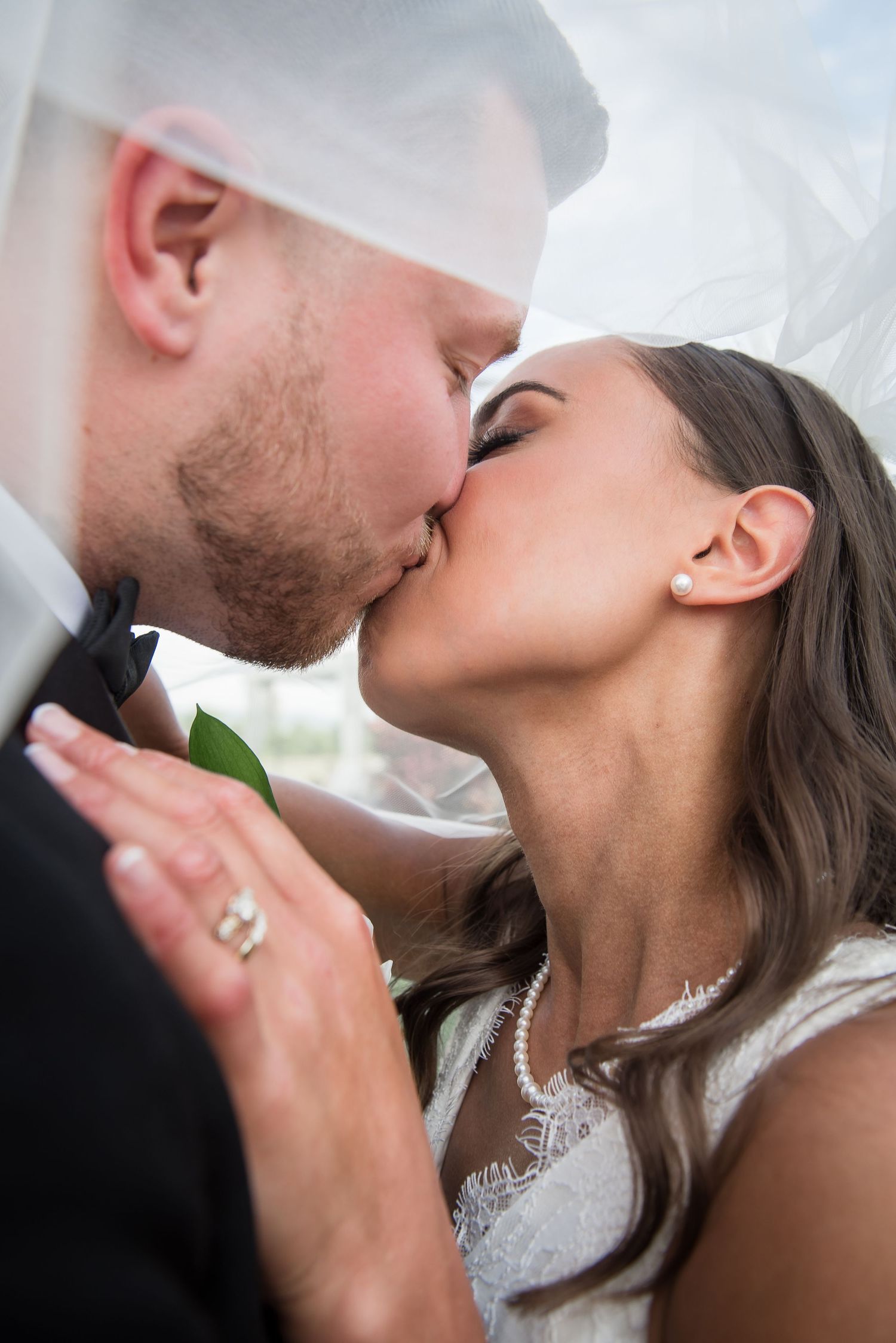 Smiling bride in white fur coat embracing groom outdoors with city skyline in background.