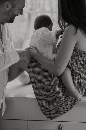 Black and white portrait of parents and small child sharing an intimate family moment on a drawer unit.
