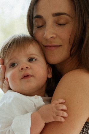 A serene moment as a small child in white rests against an adult in a warm embrace.