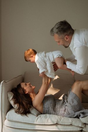Parent and baby in white shirts share playful bonding moments while lying on gray couch in progressive shots.