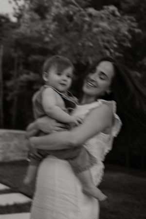 A sweet black and white moment showing a mother cradling her baby outdoors with a joyful expression.