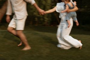 Motion-blurred photo of people playfully running together on grass in casual summer attire.