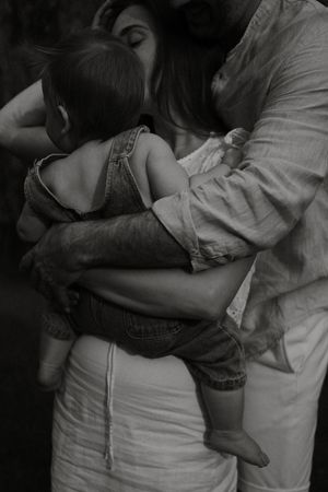 Intimate black and white photograph of parents embracing their toddler in casual denim and white clothing.